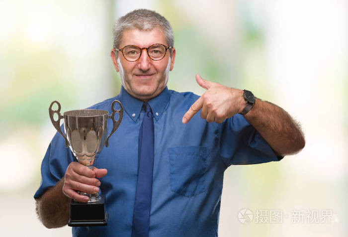 英俊的资深成功人士拿着奖杯脸上带着惊讶的表情指着自己