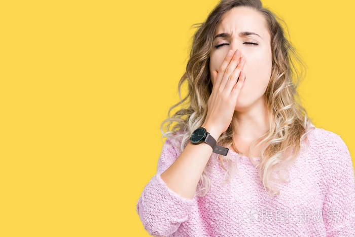 美丽的年轻金发女人在孤立的背景下无聊地打哈欠,疲惫地用手捂住嘴.