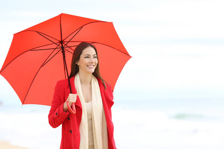 下雨天，穿红衣服的快乐女人拿着雨伞在海滩上散步