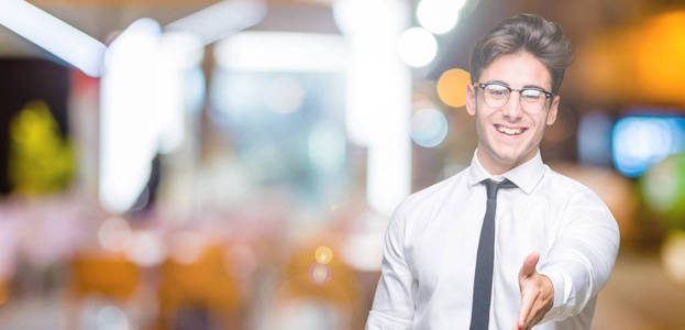 年轻的商人戴着眼镜，在孤立的背景上微笑，友好地提供握手作为问候和欢迎。 成功的生意。