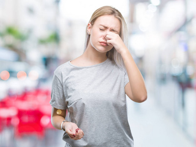 年轻的金发女人在孤立的背景上闻到一些臭味和令人恶心的难以忍受的气味，用手指在鼻子上屏住呼吸。 难闻的概念。