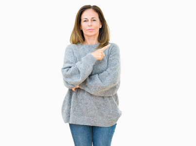 美丽的中年妇女穿着冬天的毛衣，在孤立的背景上，用手指着一边，显示出广告严肃而平静的脸