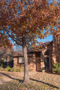 美国德克萨斯州花丘，有五颜六色秋叶的单身家庭住宅入口。 在阳光明媚的秋天，门廊和海湾窗户上有季节性的花环，地上有叶子
