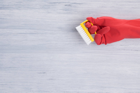 用红色橡胶手套手持刷子清洁表面，在灰色背景下，有刻字的空间。