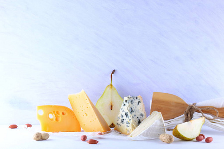 白色背景下的各种奶酪梨和花生。羊皮纸上的蓝奶酪和香豆。早餐用乳制品和水果。健康食品