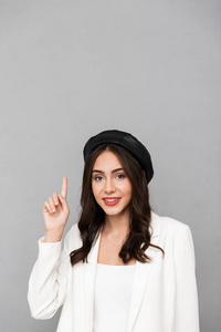 一个微笑的年轻女子的肖像，戴着贝雷帽，站在灰色背景上，孤立地指着上面