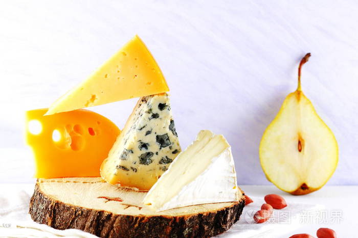 奶酪，梨和花生放在木架上。白色餐巾纸上的硬黄色奶酪和卡姆伯特。早餐用乳制品和水果。健康食品