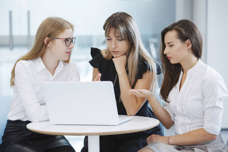 办公室工作人员队伍..三位商界女性坐在一张桌子上，手提电脑，正在计划未来的企业发展理念。