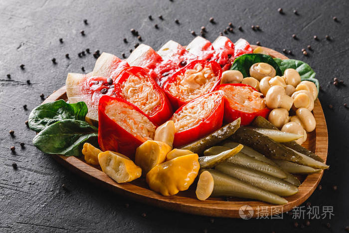 各种腌制蔬菜，泡菜，卷心菜，西瓜，黄瓜，蘑菇和草药在木板上的深色石头背景。 小吃和葡萄酒开胃菜。 俯视图平躺