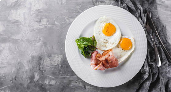 早餐煎鸡蛋，培根，火腿，新鲜沙拉，盘子上的灰色桌子表面。 健康食品顶层平躺