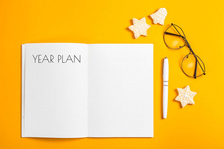 年计划写在一个笔记本上，上面写着干净的床单，放在钢笔旁边，用白色的图案装饰着冬天的饼干。规划新的一年概念..俯视图，平躺