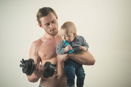 健康的家庭生活方式。父亲和孩子一起训练。强壮的男人和男婴和哑铃。父子建造二头肌。活跃的家庭喜欢运动和健身。体育迷