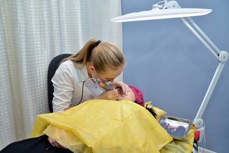 美容师一位穿白色长袍的医生在美容院做永久唇妆的过程中治疗一个年轻女孩的嘴唇。 肖像。 快关门。 水平视图。