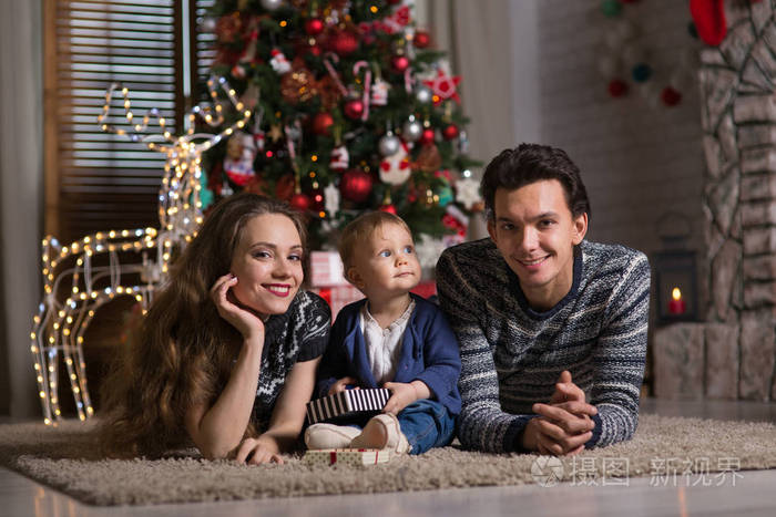 一家人坐在圣诞树旁,孩子一岁,一个年轻的女人和一个男人在等圣诞节