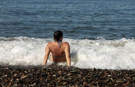 穿着蓝色泳衣的女人坐在海滩上的海边看到海浪