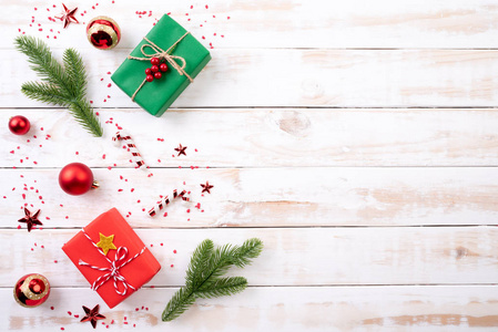 圣诞节背景概念。 顶部的圣诞绿色和红色礼品盒与云杉枝，松果，红色浆果和铃铛在白色的木制背景。