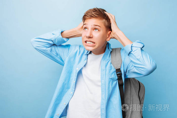 情绪低落的青少年男子举起双手,绝望地在蓝色背景上发出恼人的面部