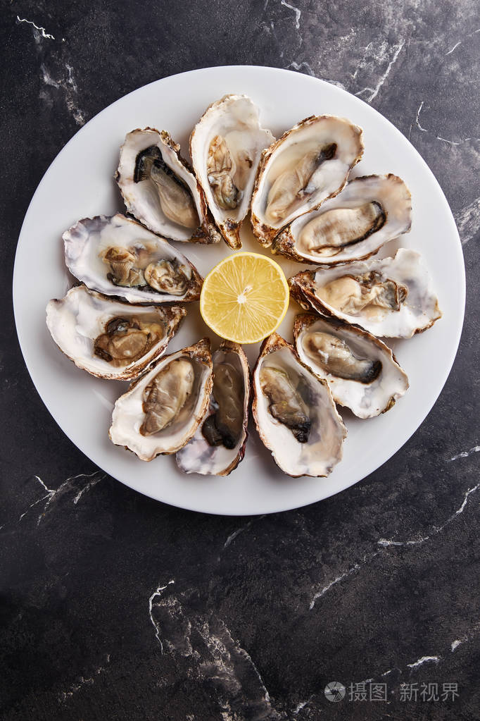 新鲜开放的牡蛎用柠檬片放在黑色大理石桌上的白色盘子里