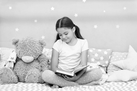 睡觉前看书。女孩的孩子坐在床上, 泰迪熊看书。孩子准备上床睡觉。在舒适的卧室愉快的时间。小女孩长头发可爱的睡衣放松和读书熊玩具