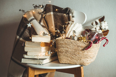 冬天温暖的毯子放在椅子上, 上面有一篮子圣诞装饰品书和带绳灯。家。冬季阅读。房子