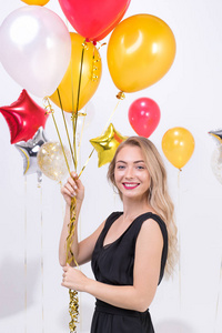 美丽的年轻白种人女人穿着黑色的衣服，快乐的微笑着拿着五颜六色的气球在有趣的派对工作室肖像拍摄白色背景。
