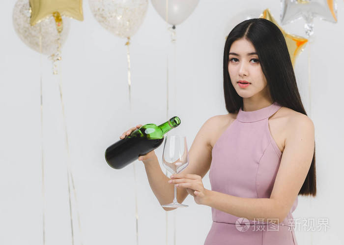 美丽的年轻亚洲女人粉红色倒酒在有趣的聚会白色背景与节日五颜六色的