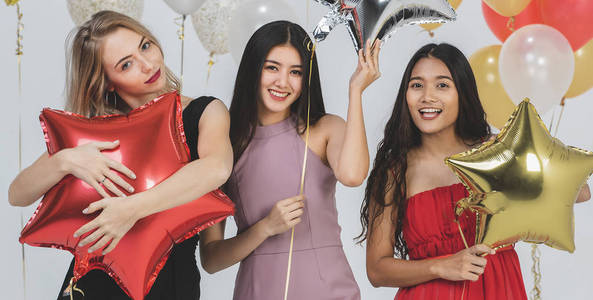 多样化的年轻快乐女性在派对上一起玩，白色背景和五颜六色的节日气球。