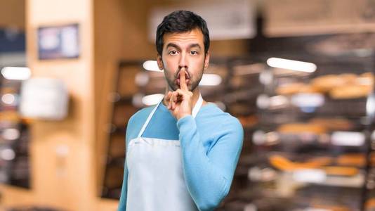 一个穿着围裙的男人在一家面包店里做了一个闭着嘴沉默的手势