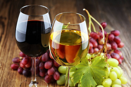 白葡萄酒和红葡萄酒在玻璃杯中，葡萄在乡村背景上掉落