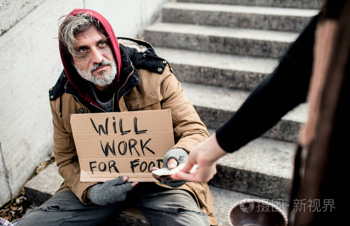 无法辨认的女人给钱无家可归的乞丐男子坐在城市