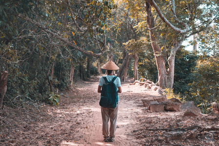 一名游客在丛林中游览吴哥窟遗址，旅游目的地柬埔寨。戴传统帽子的女人，后视图。