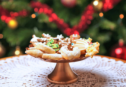 各种装饰的圣诞饼干在蛋糕架上。背景中的圣诞树。