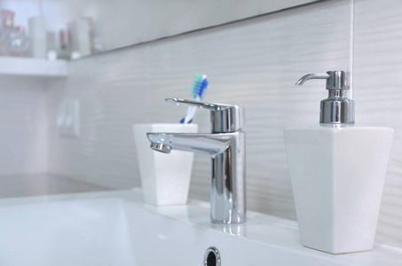 白色浴室的洗脸盆，有肥皂分配器，玻璃里有牙刷。