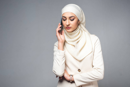 年轻的穆斯林妇女用智能手机交谈，隔离灰色