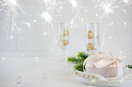 新年庆典。 银色圣诞桌设置与两个香槟杯在餐桌和礼品盒。 带着火花
