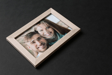 照片的幸福夫妇在框架与裂缝玻璃在黑暗的背景。 离婚概念