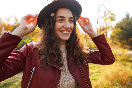 秋天，戴着帽子在公园散步的美丽微笑的年轻女子