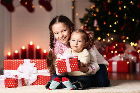 美丽的两个姐姐，带着礼品盒坐在家中的圣诞树旁