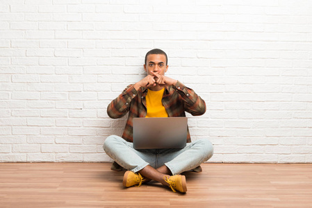 非裔美国人拿着笔记本电脑坐在地板上，表现出一种沉默的姿态