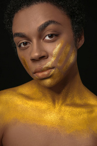 非洲裔美国妇女在黑色背景下的身体上涂着金色的颜料
