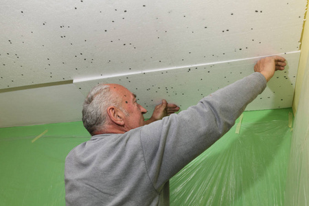工人将发泡胶保温贴在室内工程的天花板上