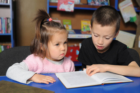 孩子们在图书馆一起学习。 小女孩在听，男孩在看书