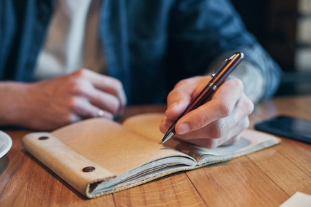 男人用笔在木桌上的笔记本上写字。特写