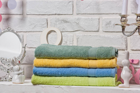 多种颜色的特里毛巾。 黄色绿色蓝色和紫色的棉毛巾。 白色砖墙背景上的纺织品。 桌子上滚动和折叠毛巾。
