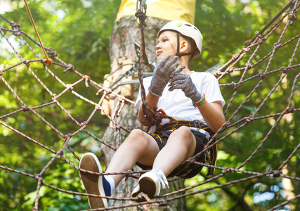 森林探险公园的孩子. 穿着白色头盔和白色t恤的孩子爬上高绳小径.