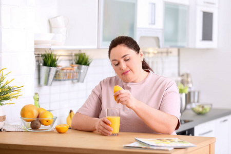 超重的女人在厨房的桌子上把橙汁倒进玻璃里。 健康饮食