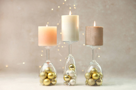 烛台上的三支燃烧的蜡烛在中性背景的木制桌子上用黄灯做了玻璃杯和圣诞球。