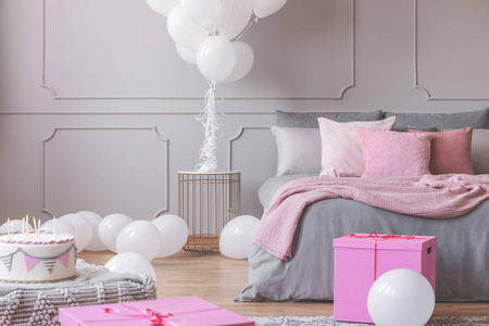 生日庆祝在卧室的一束白色气球，礼物和蛋糕在时尚的粉红色和灰色的内部真实照片