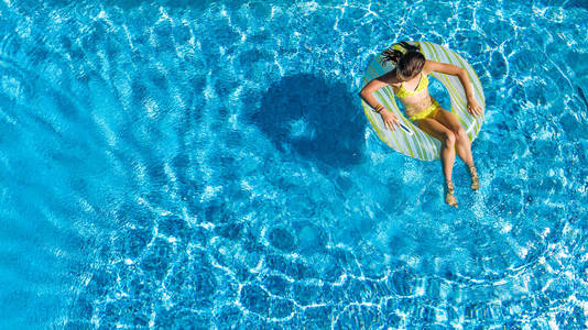 空中无人驾驶飞机观看游泳池中的小女孩从上面的孩子游泳在充气环多纳儿童在家庭度假胜地的蓝色水中玩