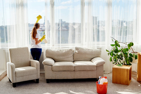 妇女在橡胶手套清洁窗口与清洁剂喷雾和黄色抹布在家里复制空间后视图。 家务和家务观念